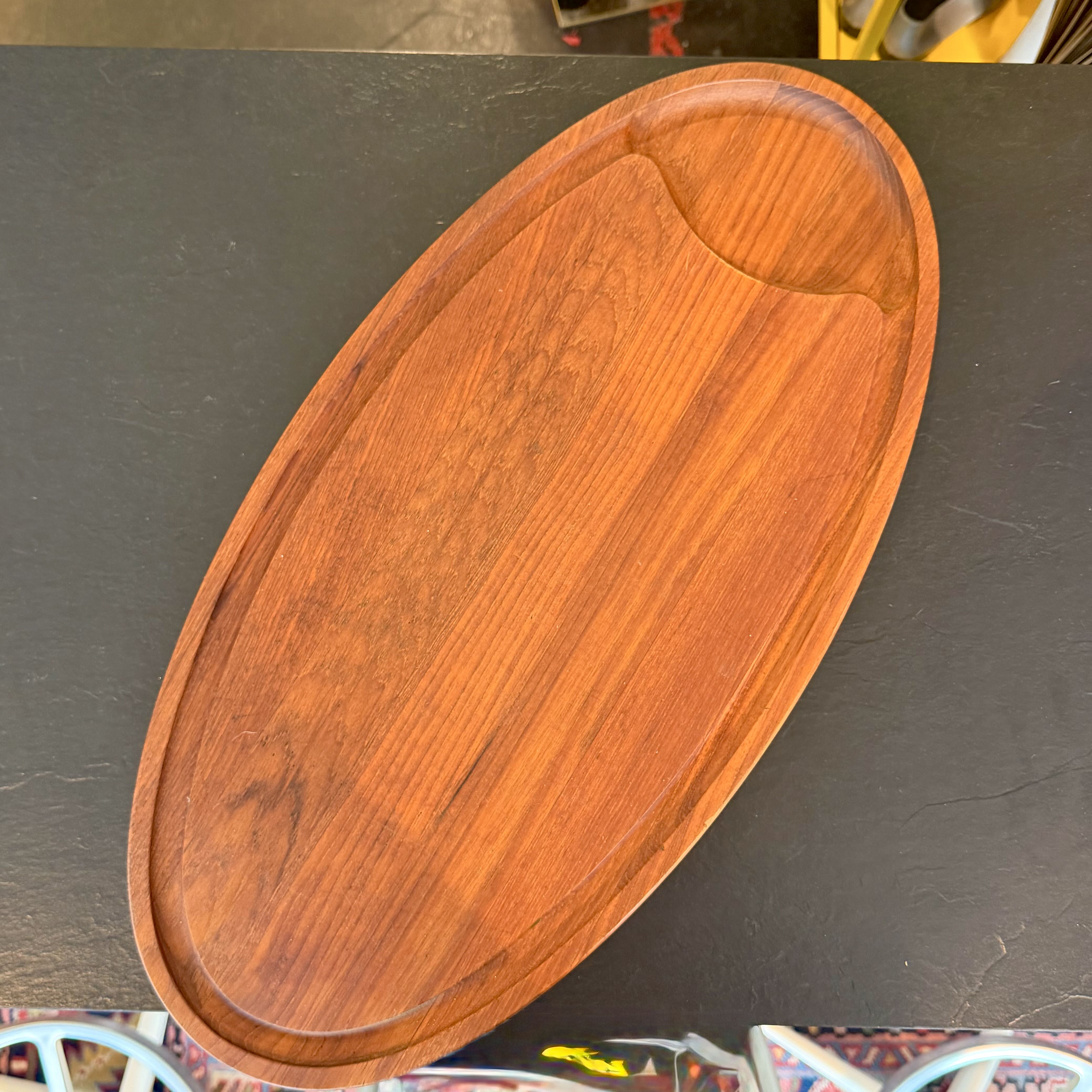 An oval wooden serving tray with a warm reddish-brown finish and visible wood grain, photographed from above on a dark tabletop.