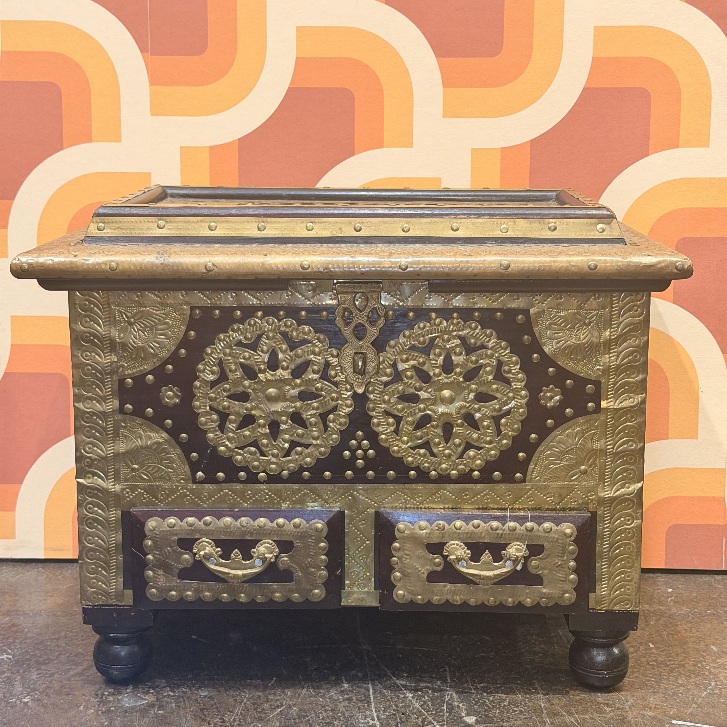 Decorative chest with intricate designs against a patterned wall.
