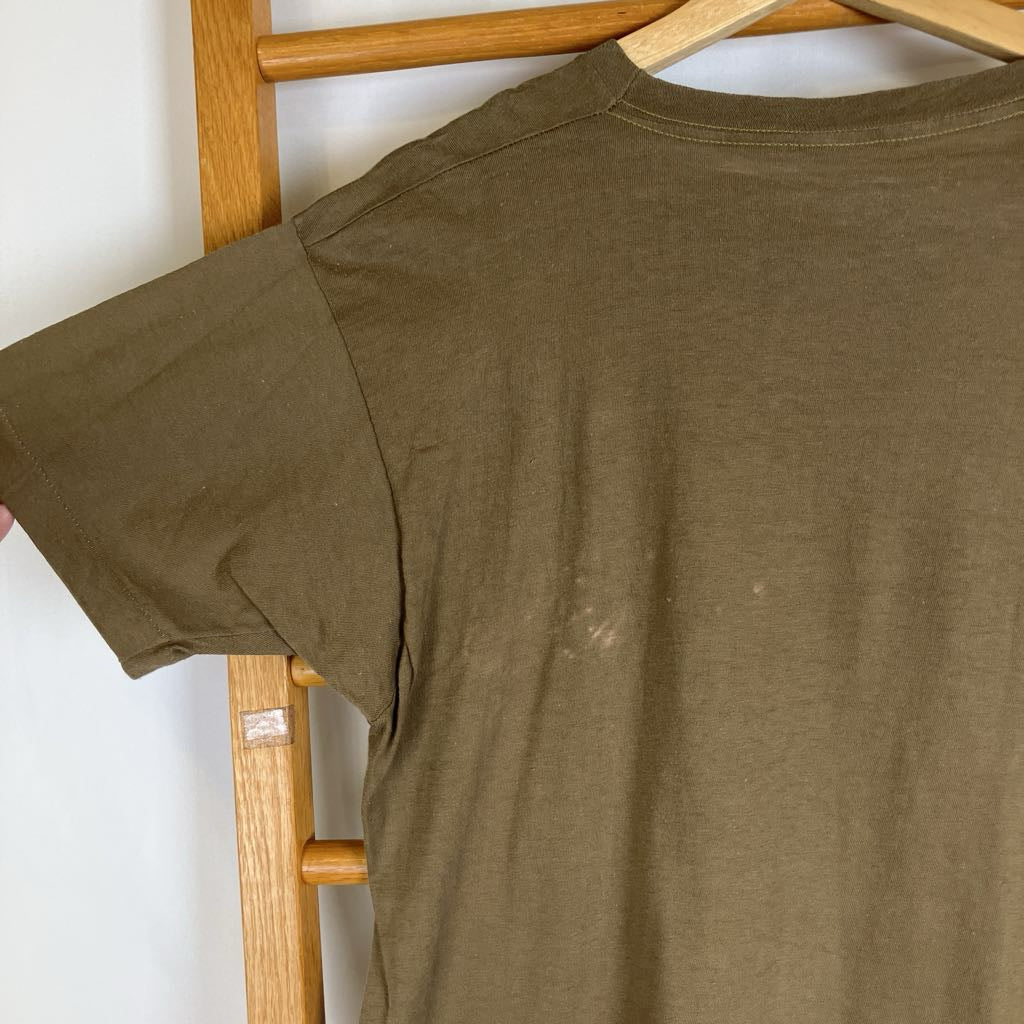 An olive green short-sleeve t-shirt hanging on a wooden hanger from a wooden clothes rack against a white wall.