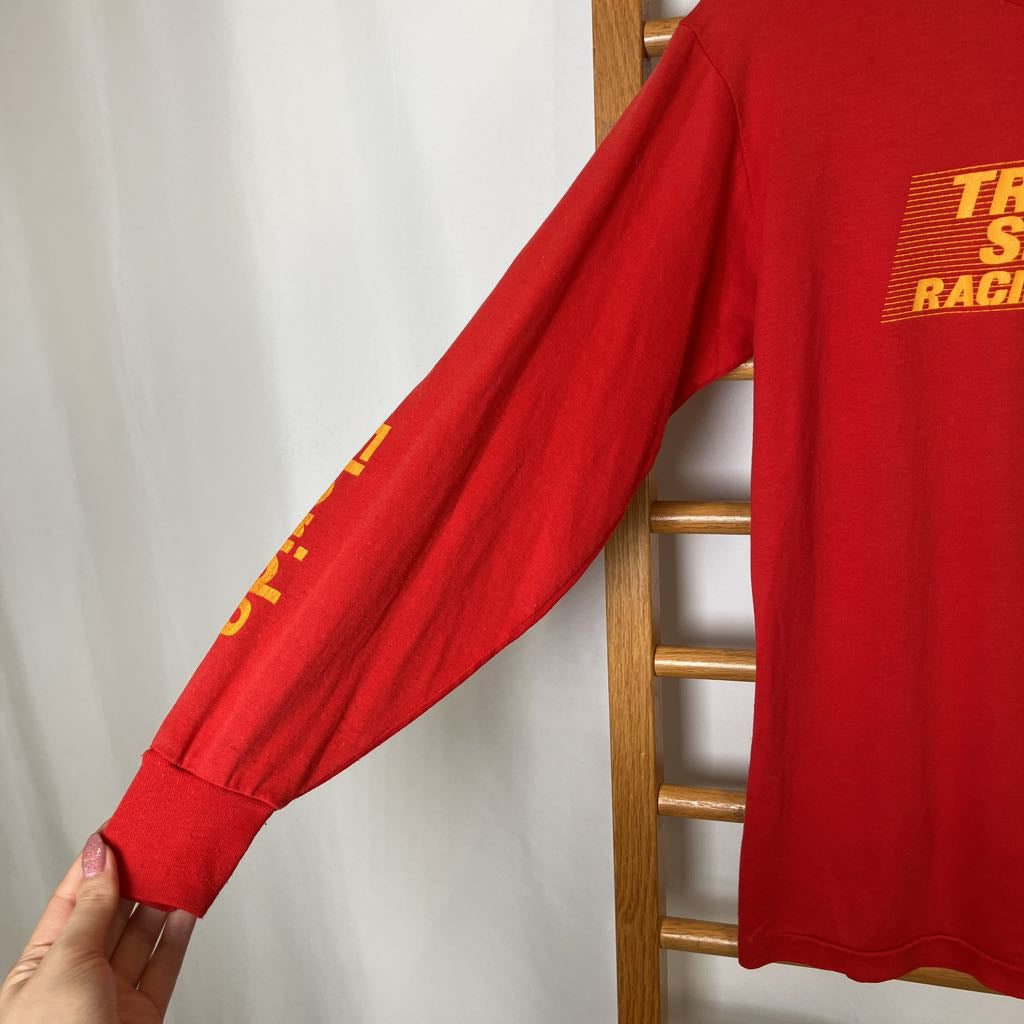 Red long-sleeve shirt with yellow text on a wooden chair against a white background