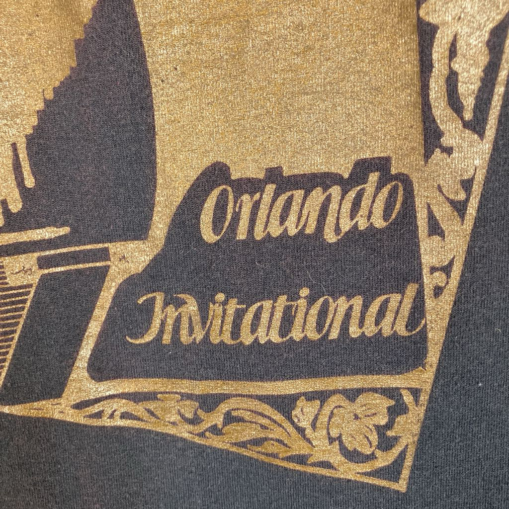 Close-up of a dark navy or black fabric printed with ornate gold artwork and the words 'Orlando Invitational' in gold script.