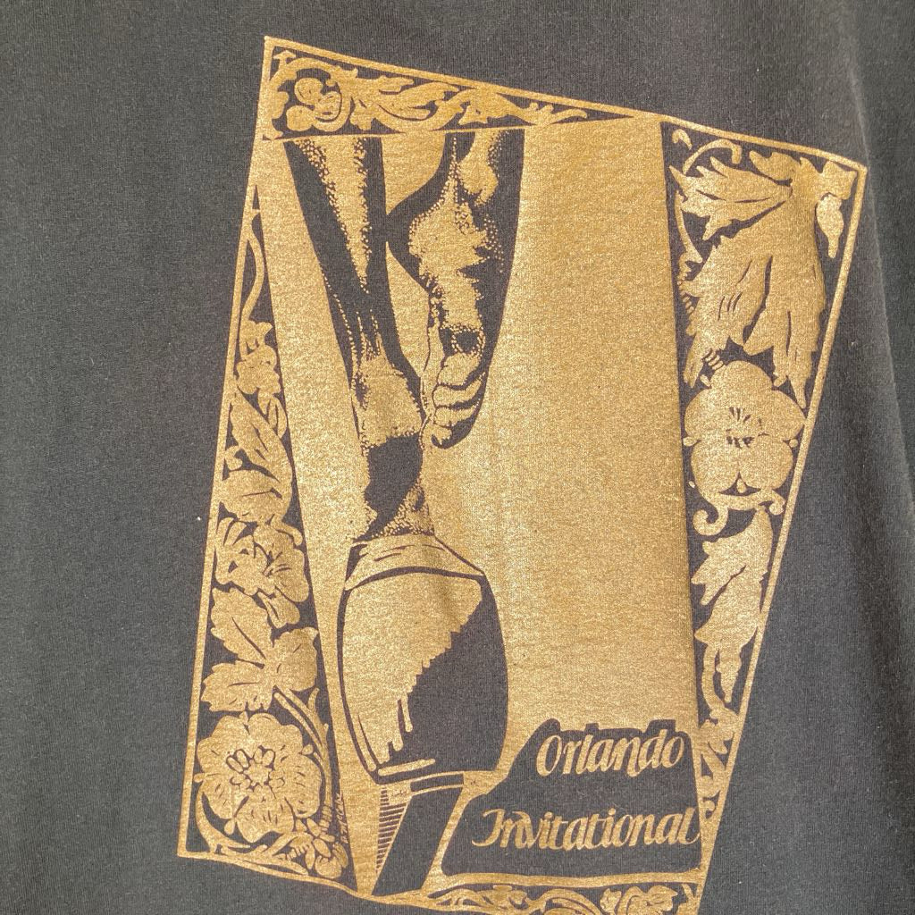 Close-up of a dark charcoal gray t-shirt featuring a vintage-style gold and black graphic print for the Orlando Invitational.