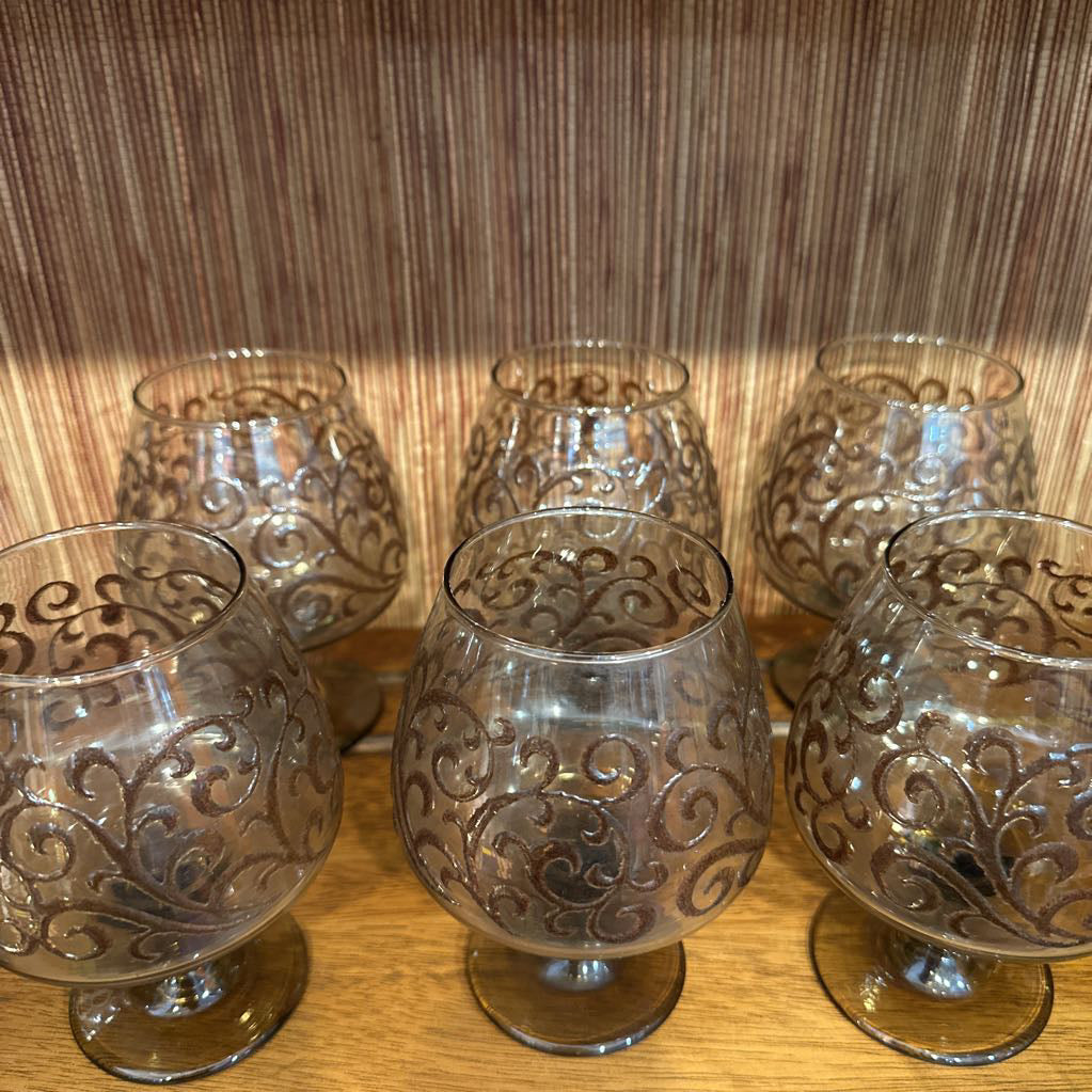 Set of six ornate glass candle holders on a wooden surface with a wooden panel background.