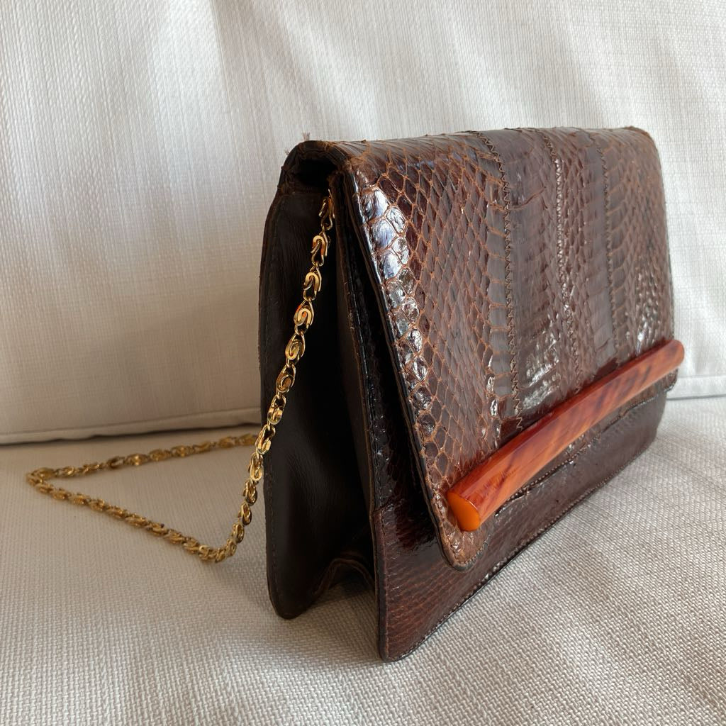 Brown leather clutch with gold chain on a light fabric background