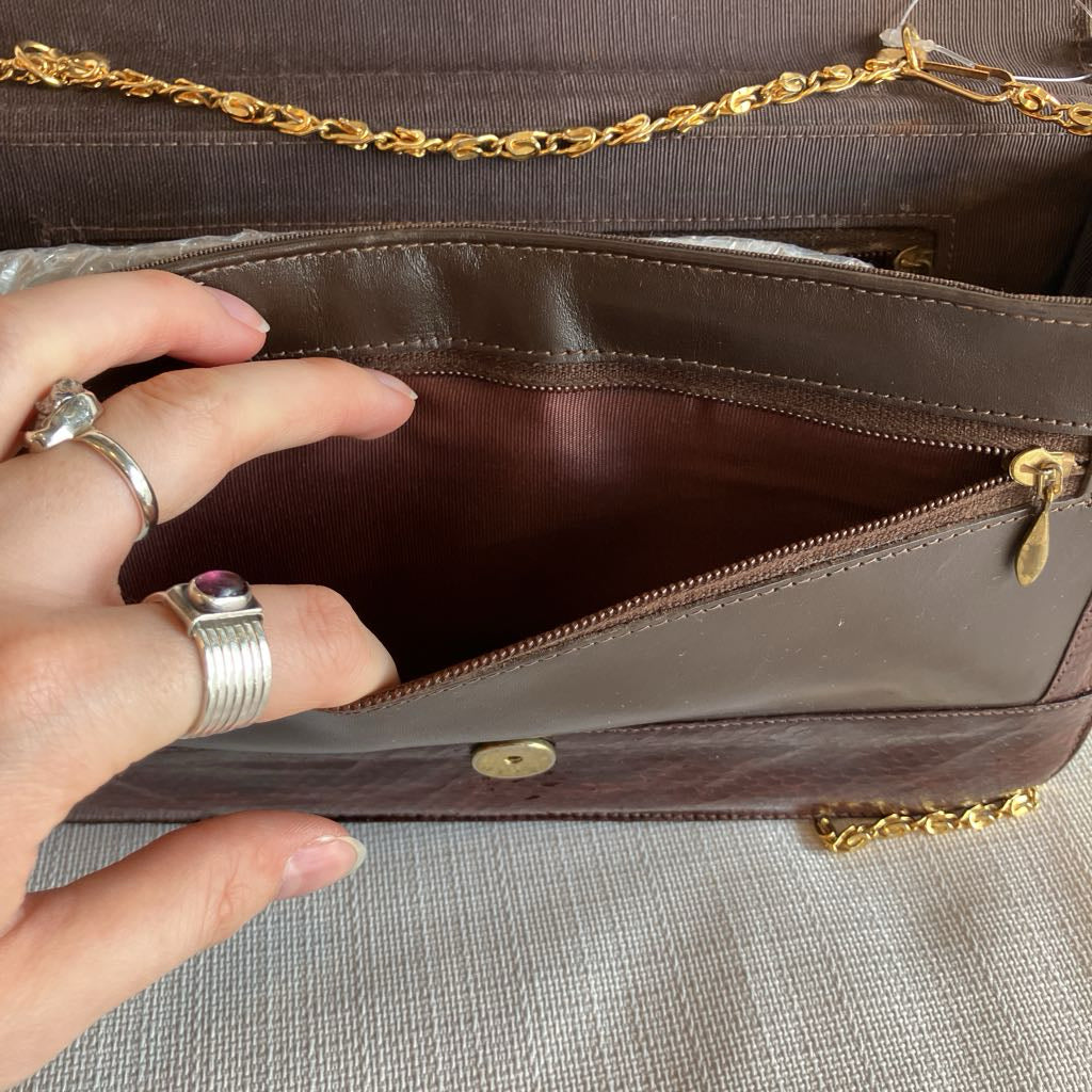 Brown leather handbag with gold chain handle, open to reveal interior, held by a hand.