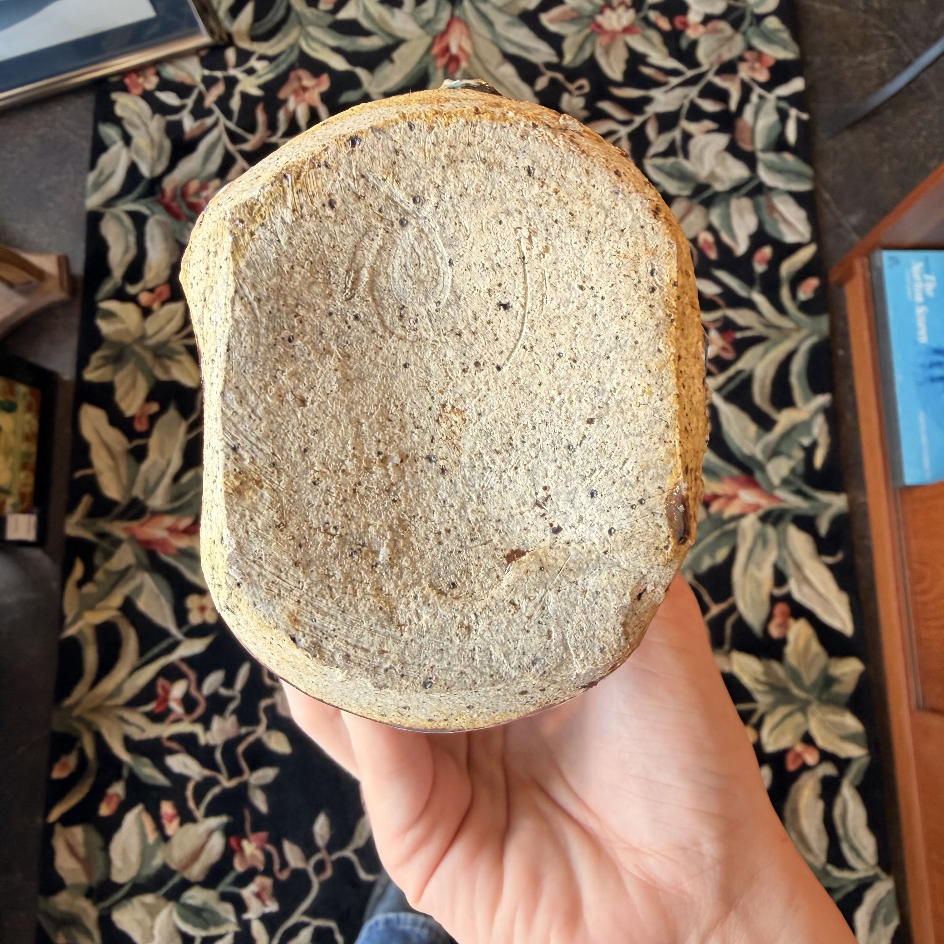 Hand holding a piece of bread with a textured surface against a patterned rug background