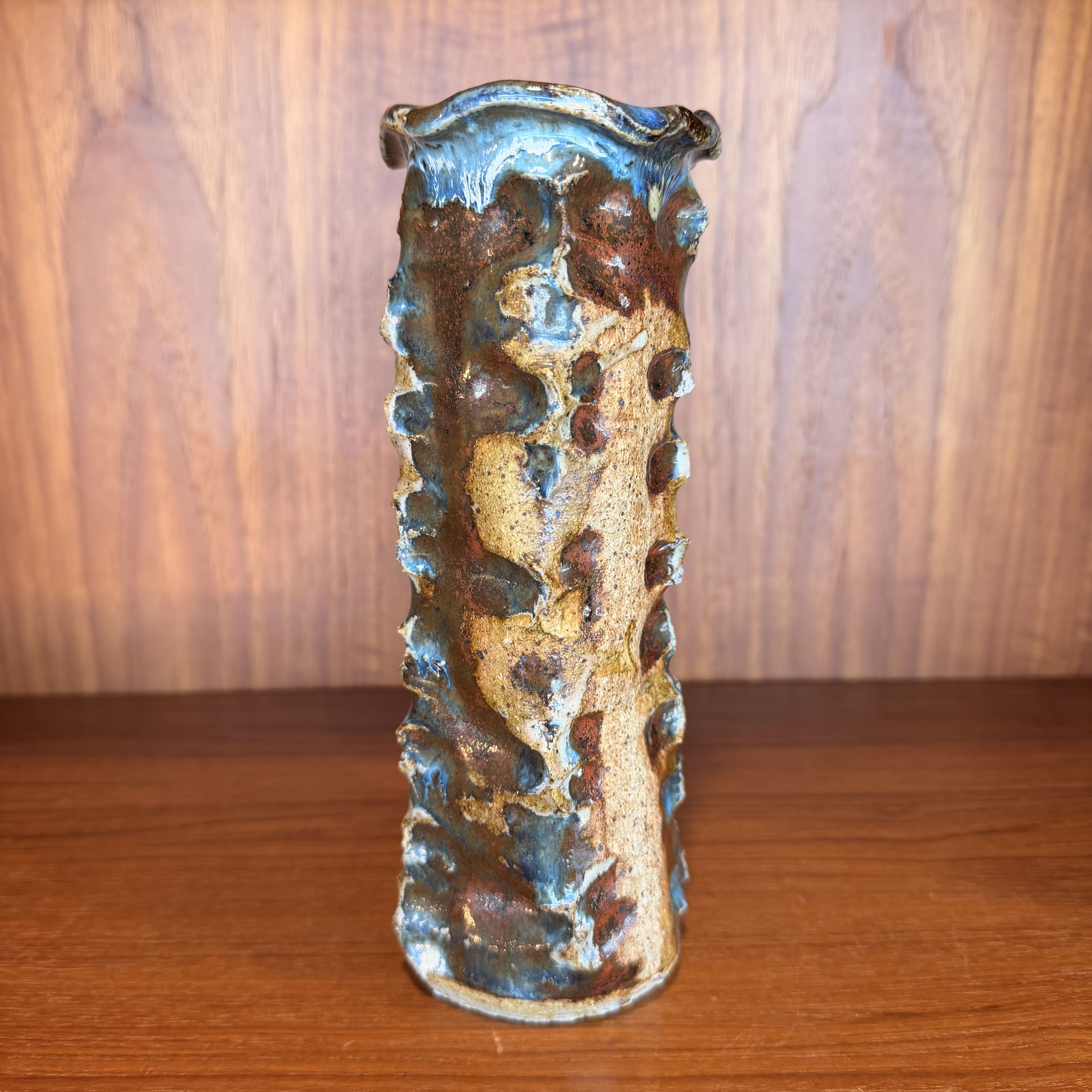 Ceramic vase with textured surface on a wooden shelf