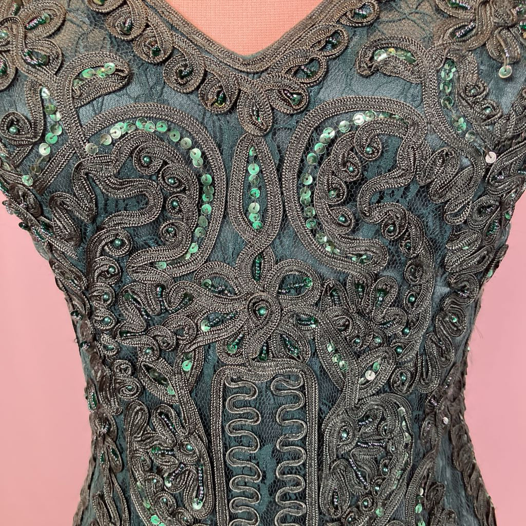 Close-up of an intricately embroidered garment with green beads on a pink background