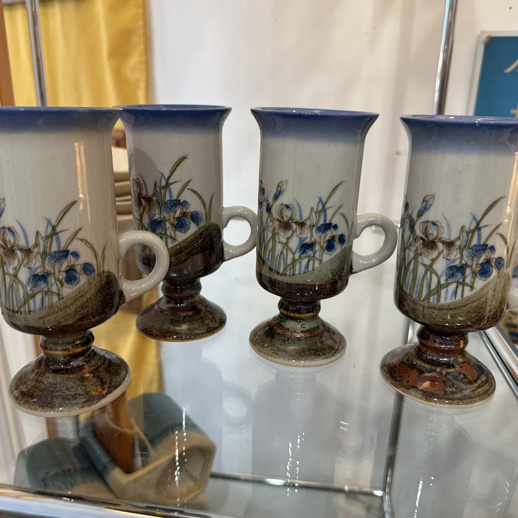 Set of four ceramic cups with floral designs on a reflective surface.
