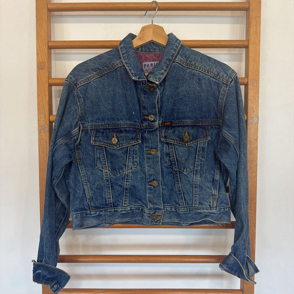 Blue denim jacket hanging on a wooden rack against a white wall