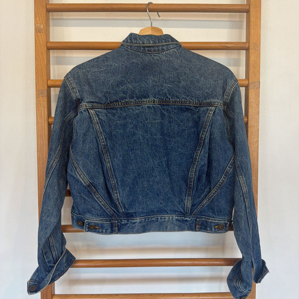 Blue denim jacket hanging on a wooden rack against a white wall