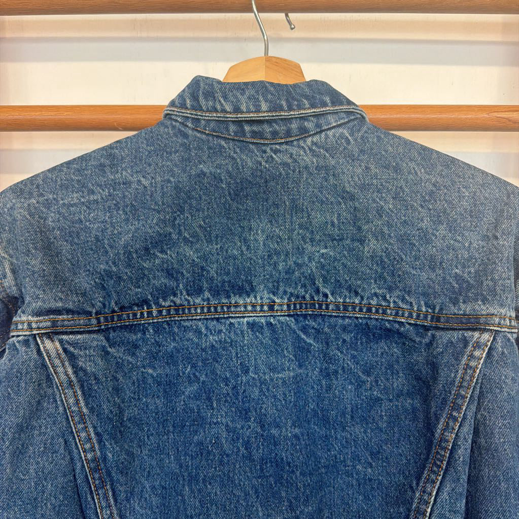 Blue denim jacket on a hanger against a neutral background