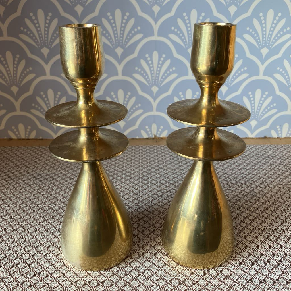 Two gold candle holders on a textured surface with a patterned wall in the background