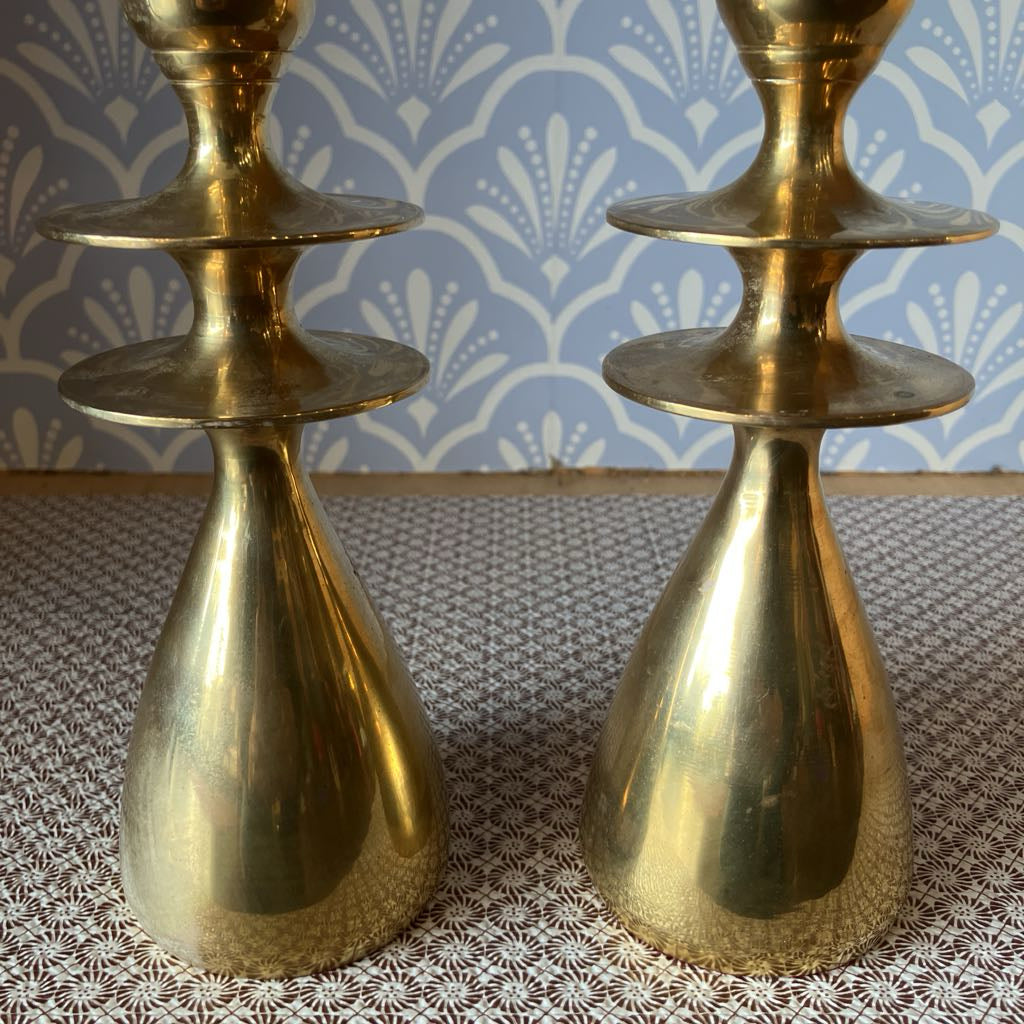 Two gold candle holders on a textured surface with a patterned blue and white background.