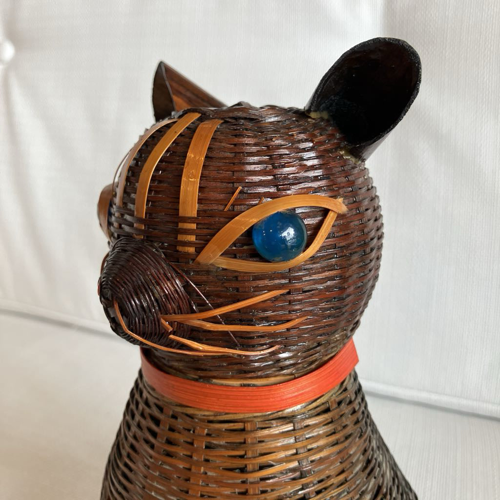 Wicker cat-shaped object with a blue eye and orange accents on a white background