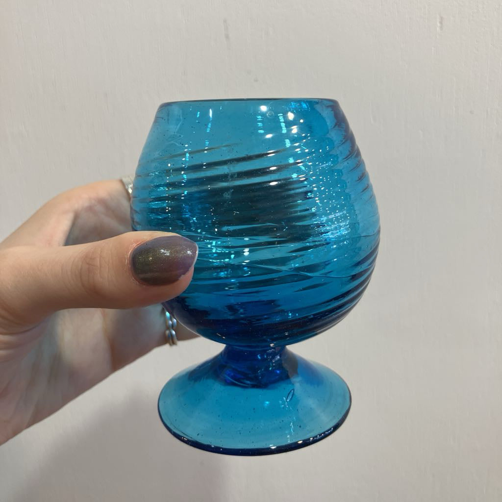 Hand holding a blue glass with a ribbed design against a plain background