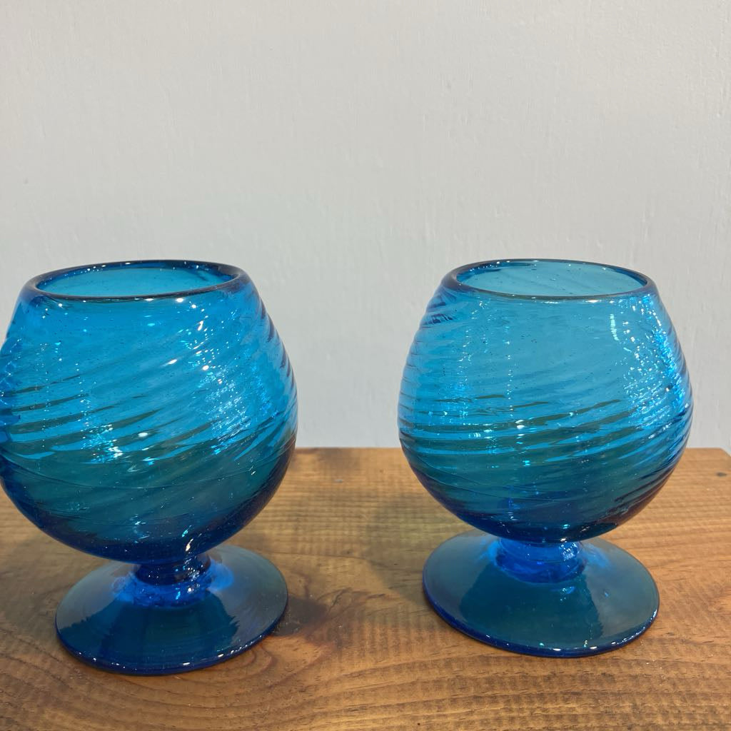 Two blue glass goblets on a wooden surface with a light gray background