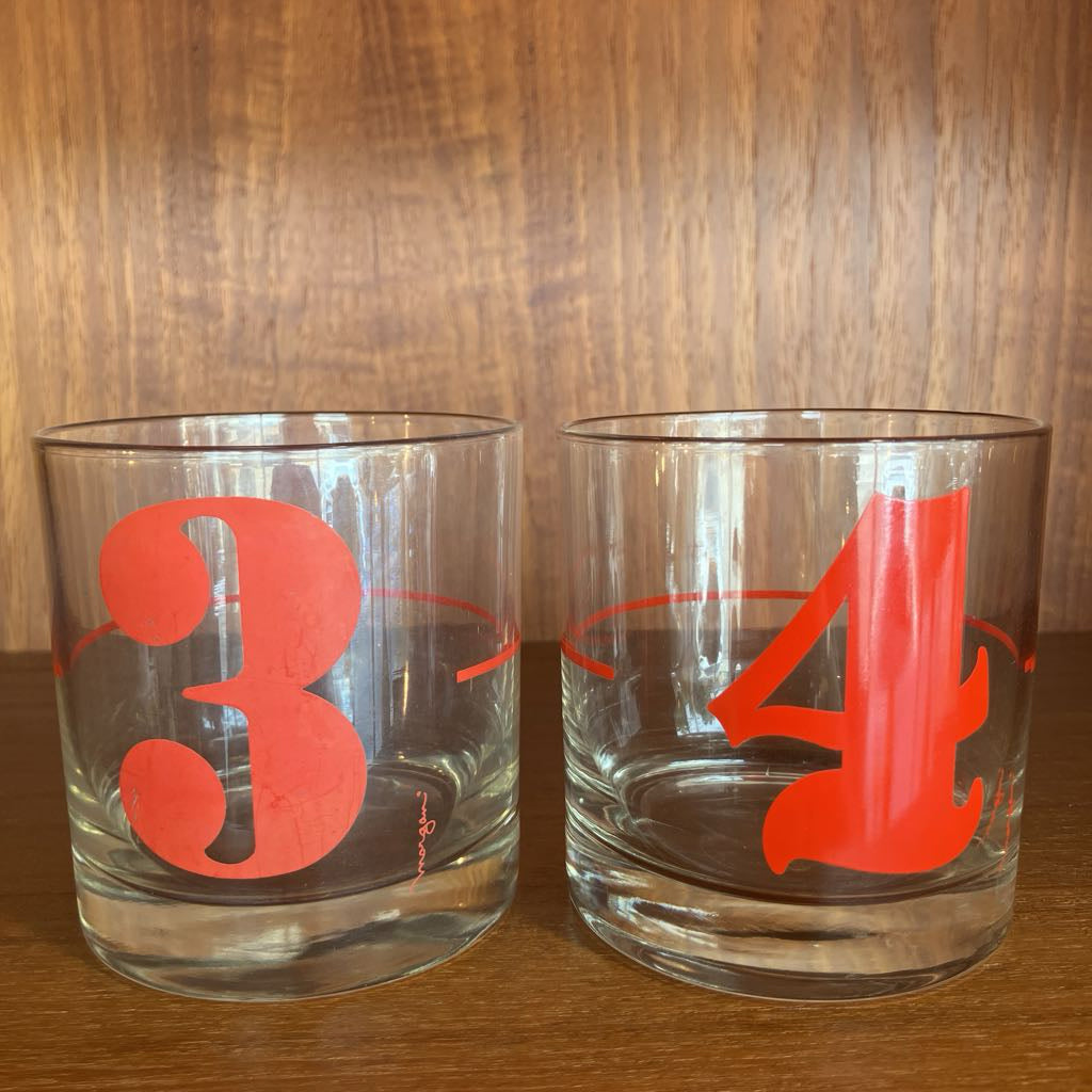 Two clear glasses with red numbers '3' and '4' on a wooden surface and background.