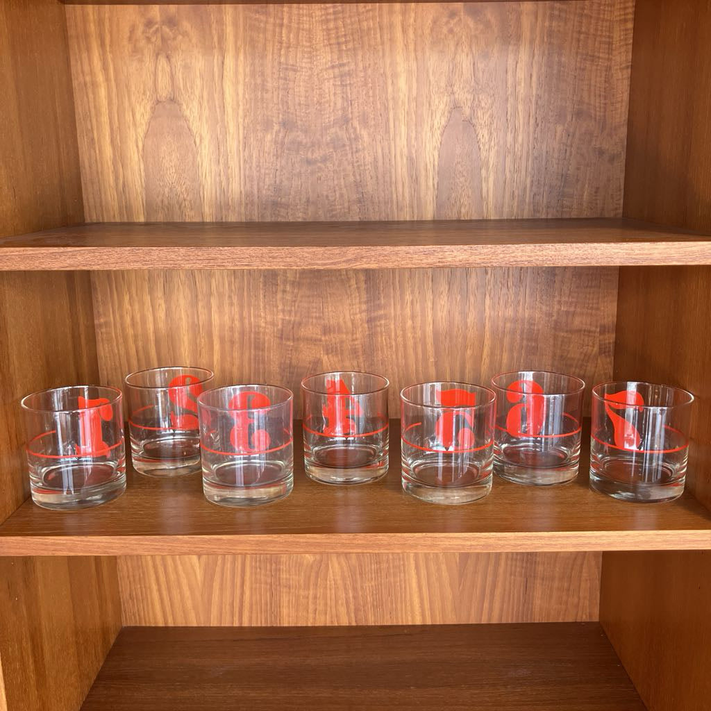 Set of clear glasses with red designs on a wooden shelf