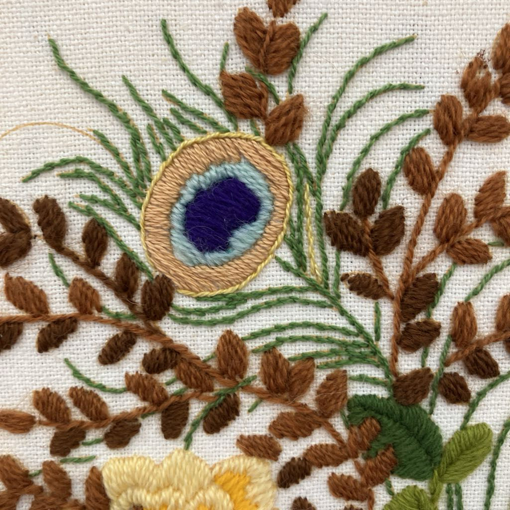 Close-up of embroidered peacock feather and foliage on fabric