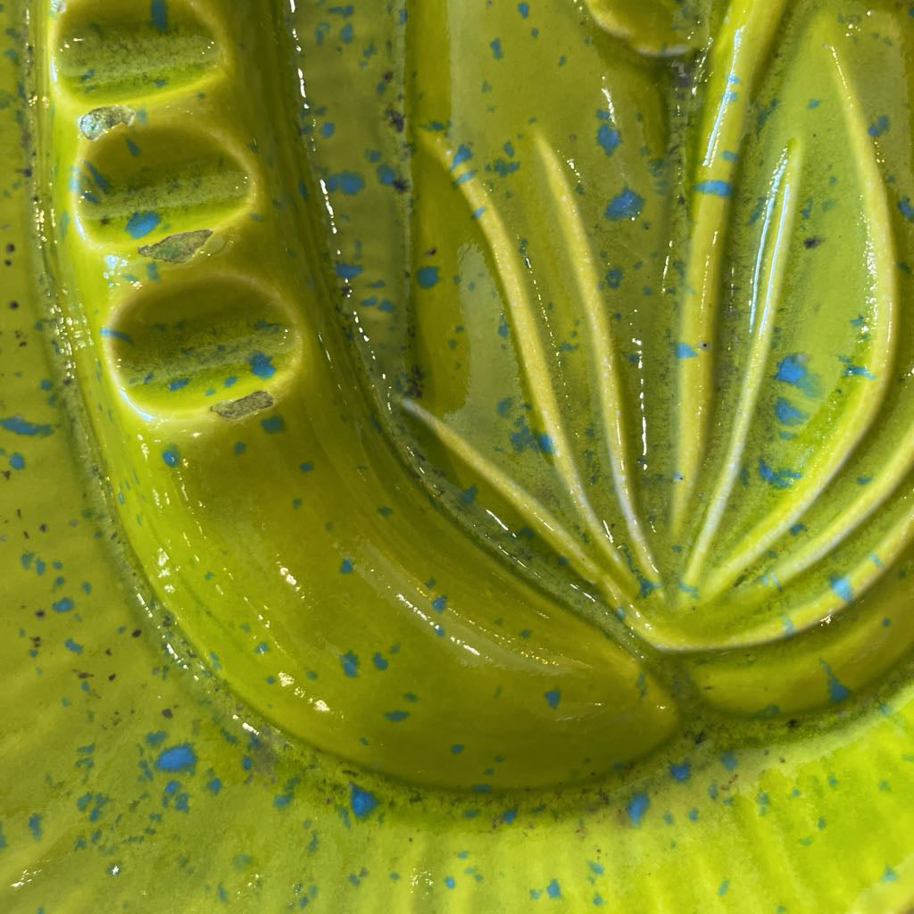 Green object with blue specks on a textured surface