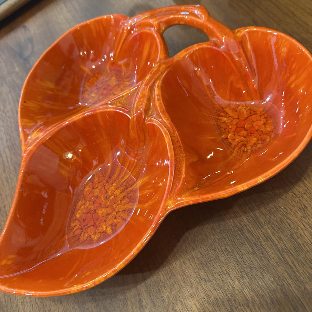 Orange ceramic leaf-shaped platter with compartments on a wooden surface