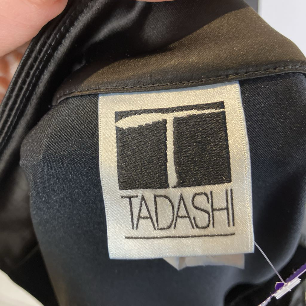 Close-up of a TADASHI label on a garment with a hand holding it.