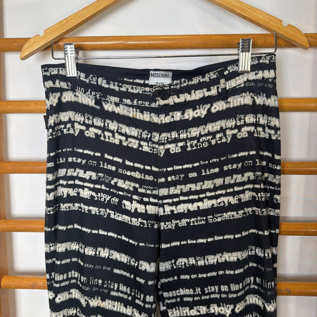Black and white patterned pants hanging on a wooden rack with 'Moschino' label.