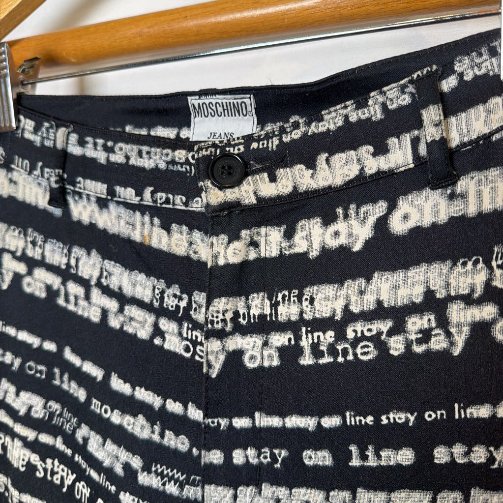 Black pants with white text pattern and Moschino label on a hanger.