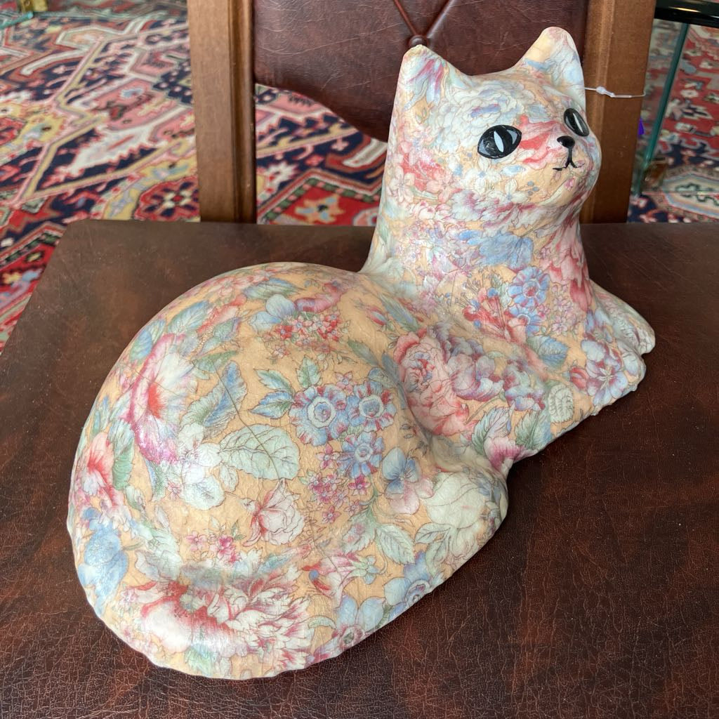 Floral-patterned cat-shaped pillow on a wooden surface with a patterned rug in the background.