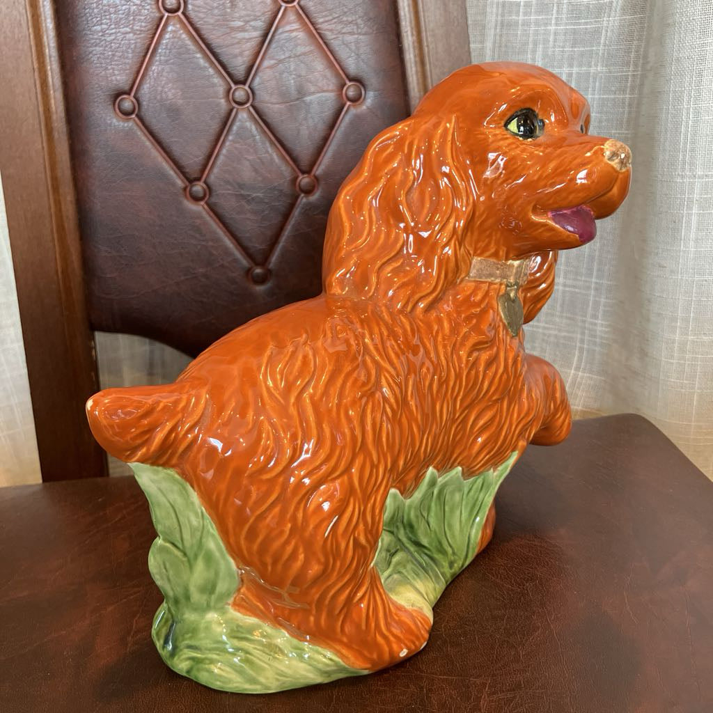Orange ceramic dog figurine on a wooden surface with a chair in the background