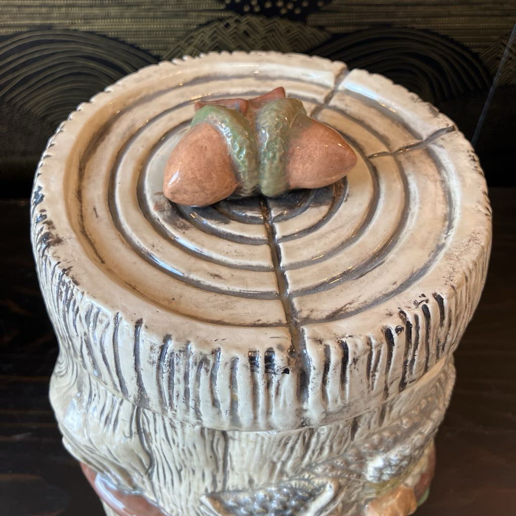 Ceramic log-shaped container with acorn decorations on a dark background