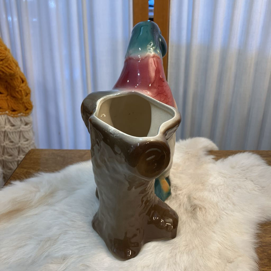 Ceramic parrot-shaped vase on a textured surface with a blurred background