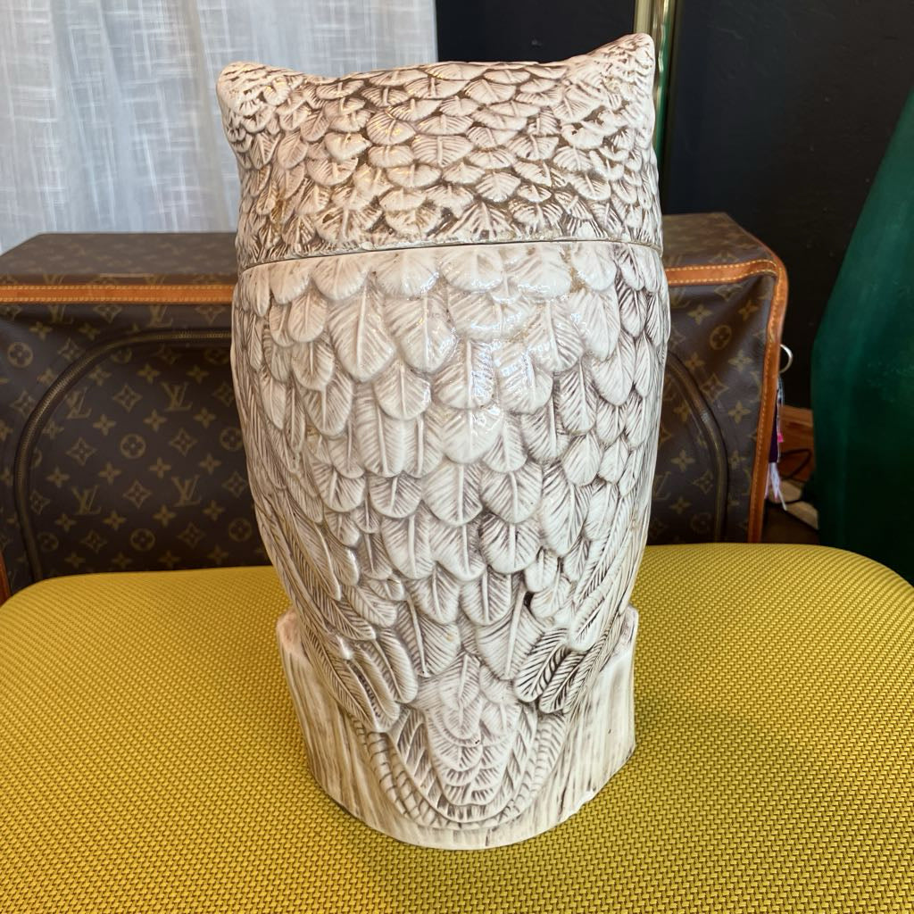 Decorative owl-shaped urn with intricate carvings on a yellow surface.