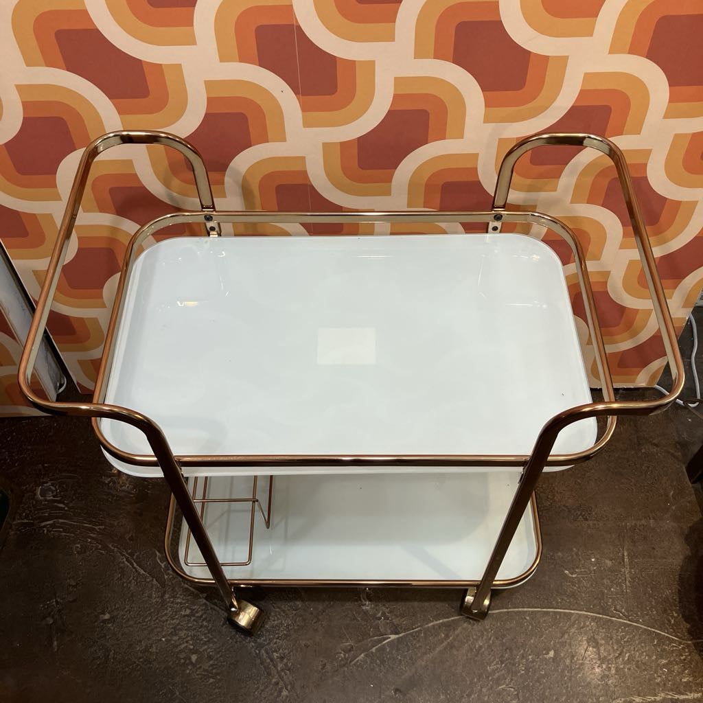 Two-tiered serving tray with gold frame against a patterned wall.