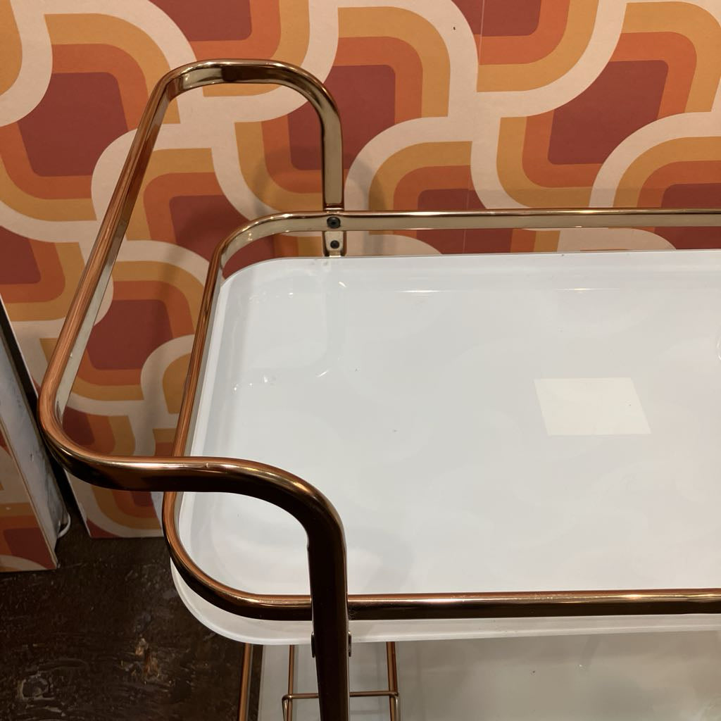 Metallic bar cart with white tray against a patterned wall