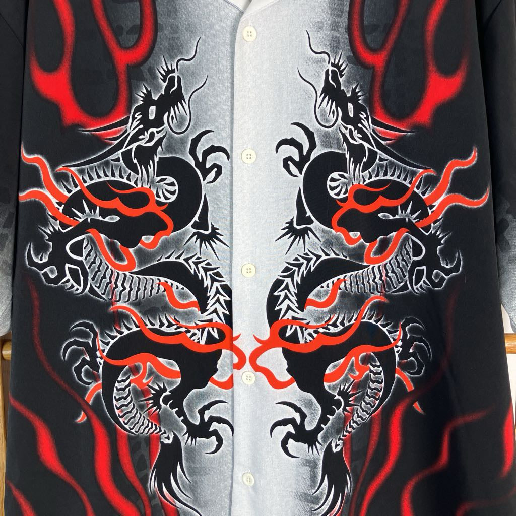 A close-up of a button-front shirt with a black base and large symmetrical dragon illustrations in white and gray, accented with vivid red flame-like lines.