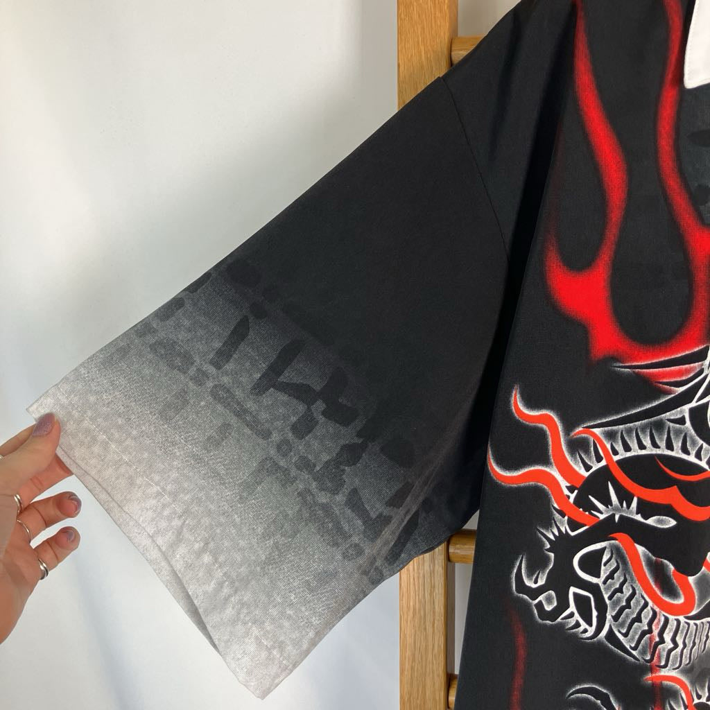 A close-up of a black wide-sleeve garment with a red and white dragon graphic and a gray gradient pattern on the sleeve, held by a hand against a white wall.