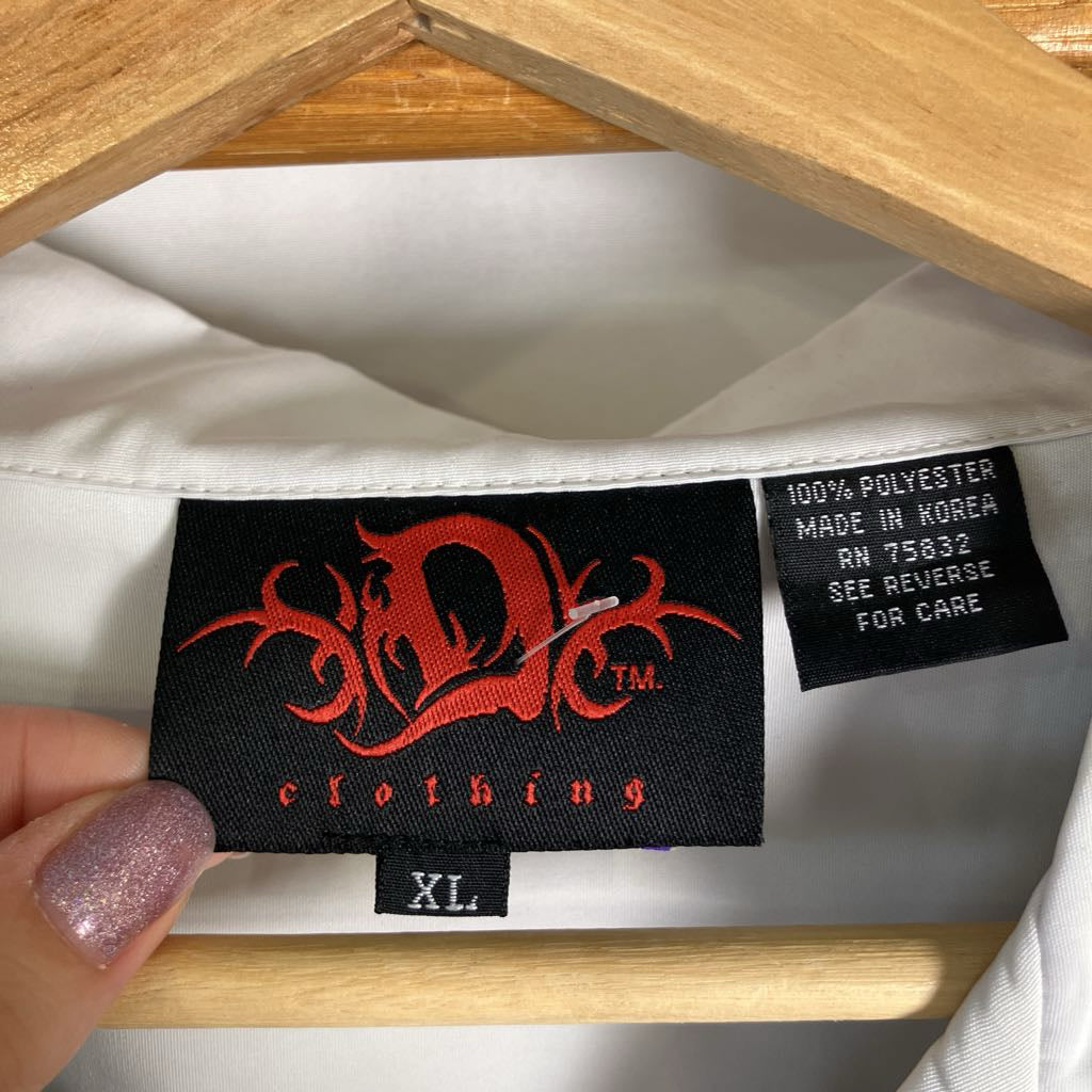 Close-up of the inside neck label of a white garment hanging on a wooden hanger, with a hand holding the left side. The label reads 'D.