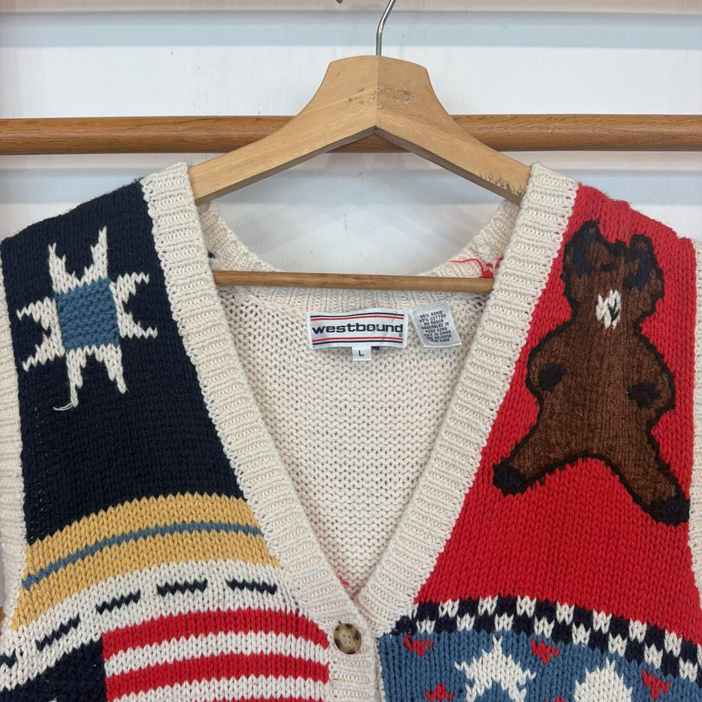 Knitted cardigan with star, stripe, and bear designs on a hanger.
