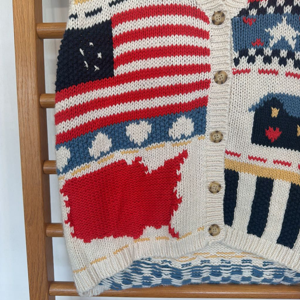 Knitted cardigan with American flag and map design on a wooden rack.