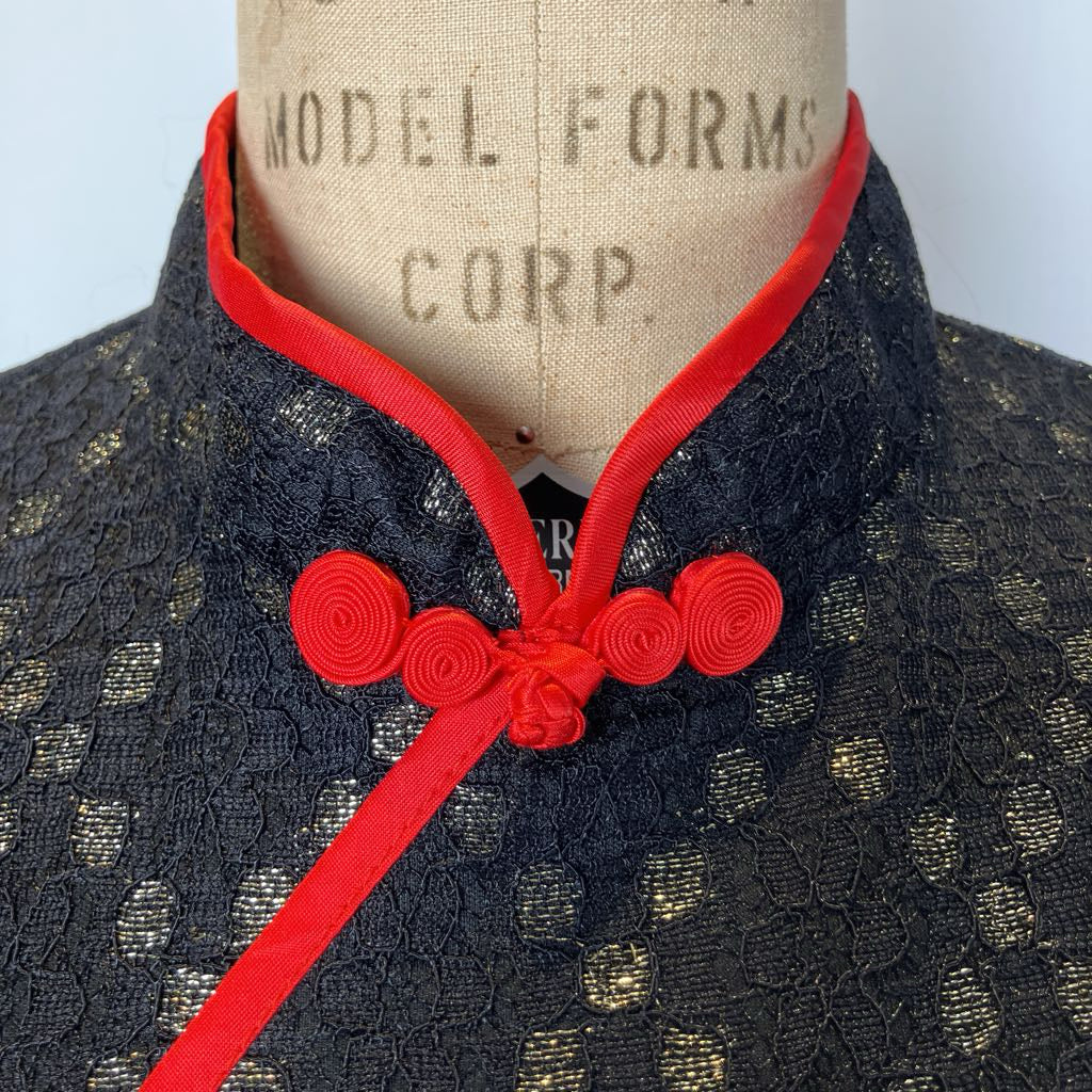 Black lace garment with red trim on a mannequin against a plain background
