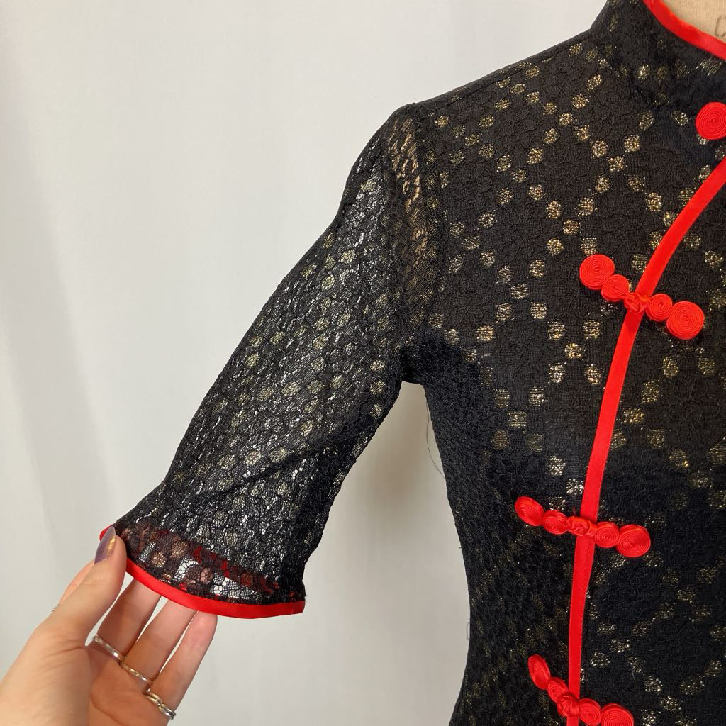 Black lace dress with red accents held by a hand against a white background