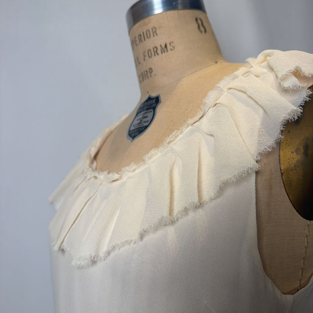 Beige blouse with ruffled neckline on a mannequin against a plain background