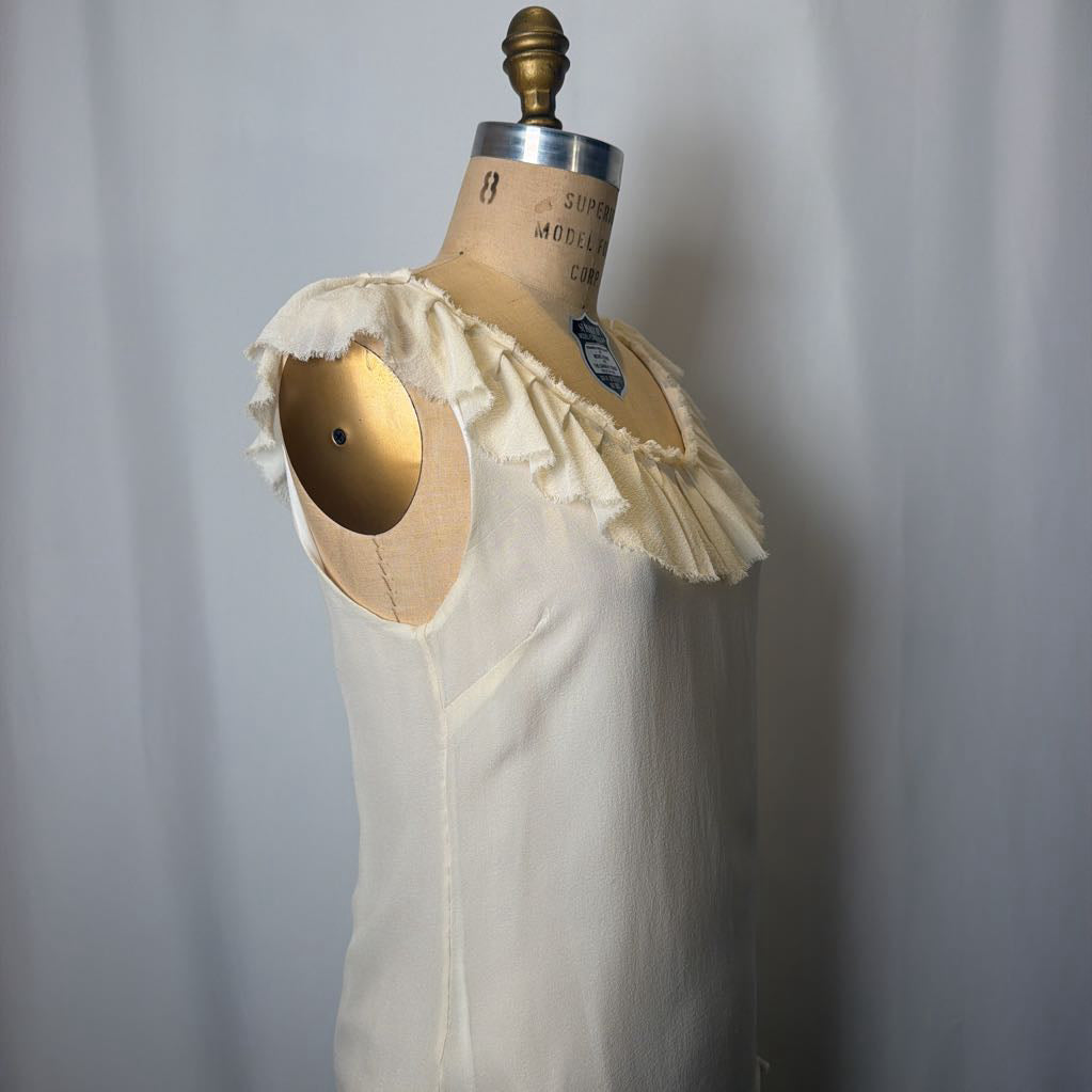 White sleeveless top with ruffled details on a mannequin against a plain background