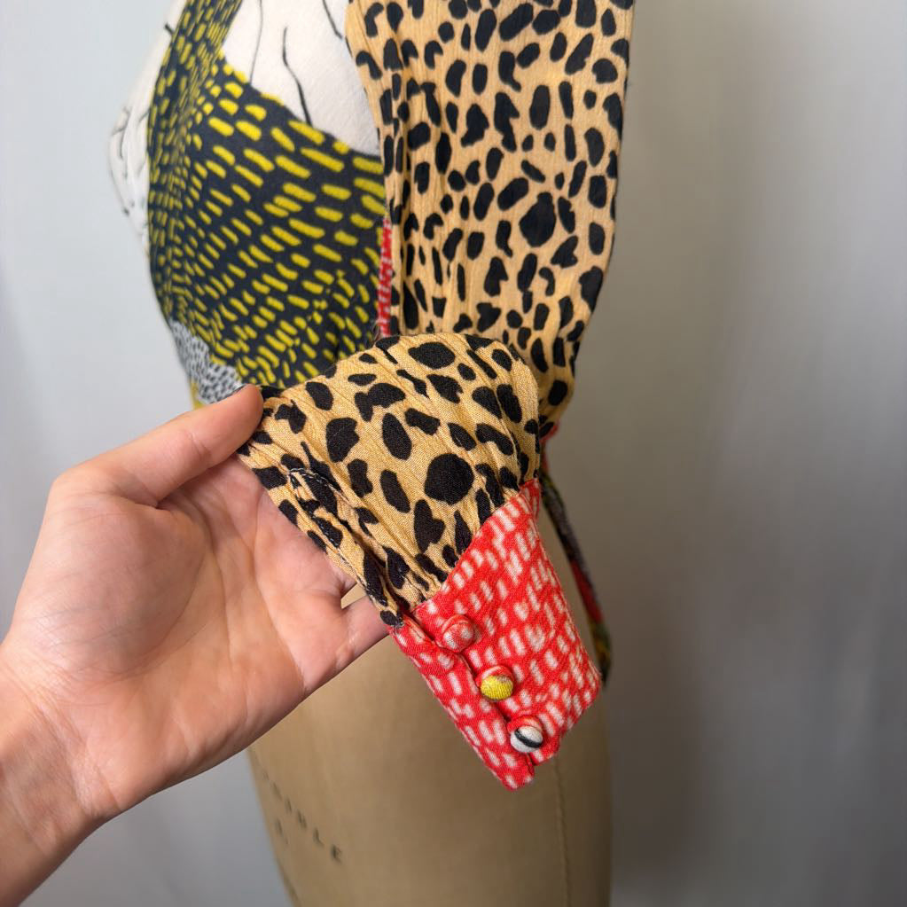 Close-up of a hand holding a fabric swatch with leopard print and red pattern, on a neutral background.