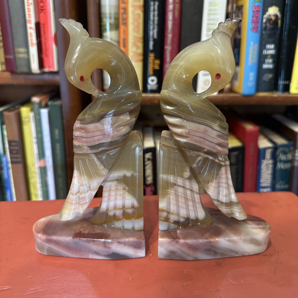 Two marbled stone sculptures of birds on a red surface with a bookshelf in the background.
