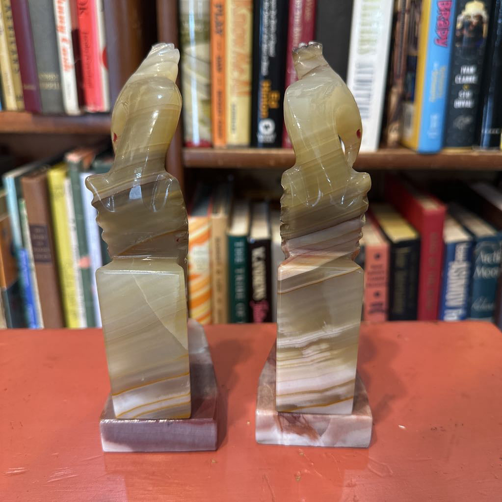 Two marble-like bookends on a red surface with a bookshelf in the background.