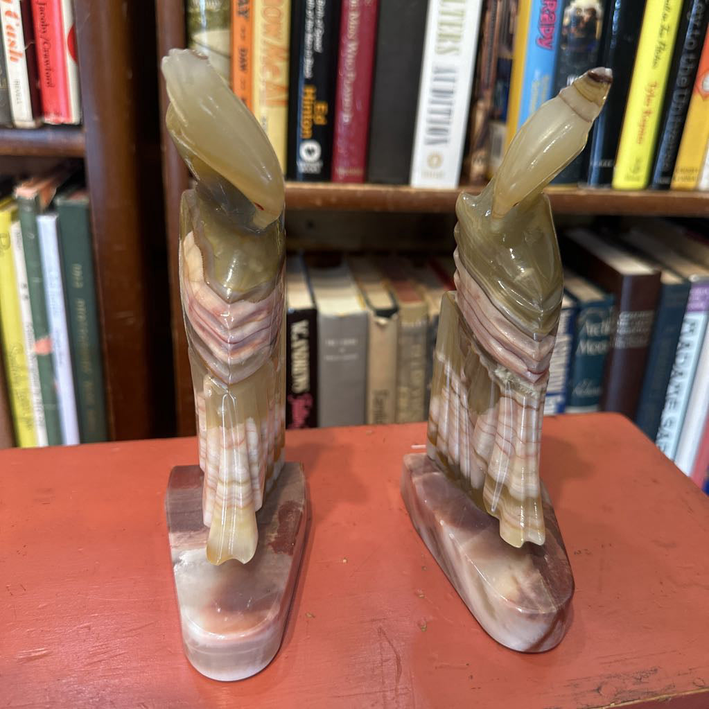 Two stone sculptures on a red surface with a bookshelf in the background