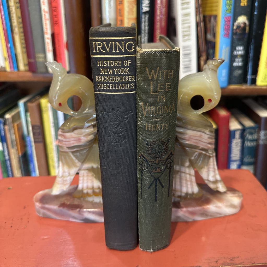 Two vintage books titled 'History of New York' and 'With Lee in Virginia' on a red surface with decorative figurines.